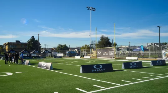 Football field surrounded by several black Oakley signs and a few constituents. 