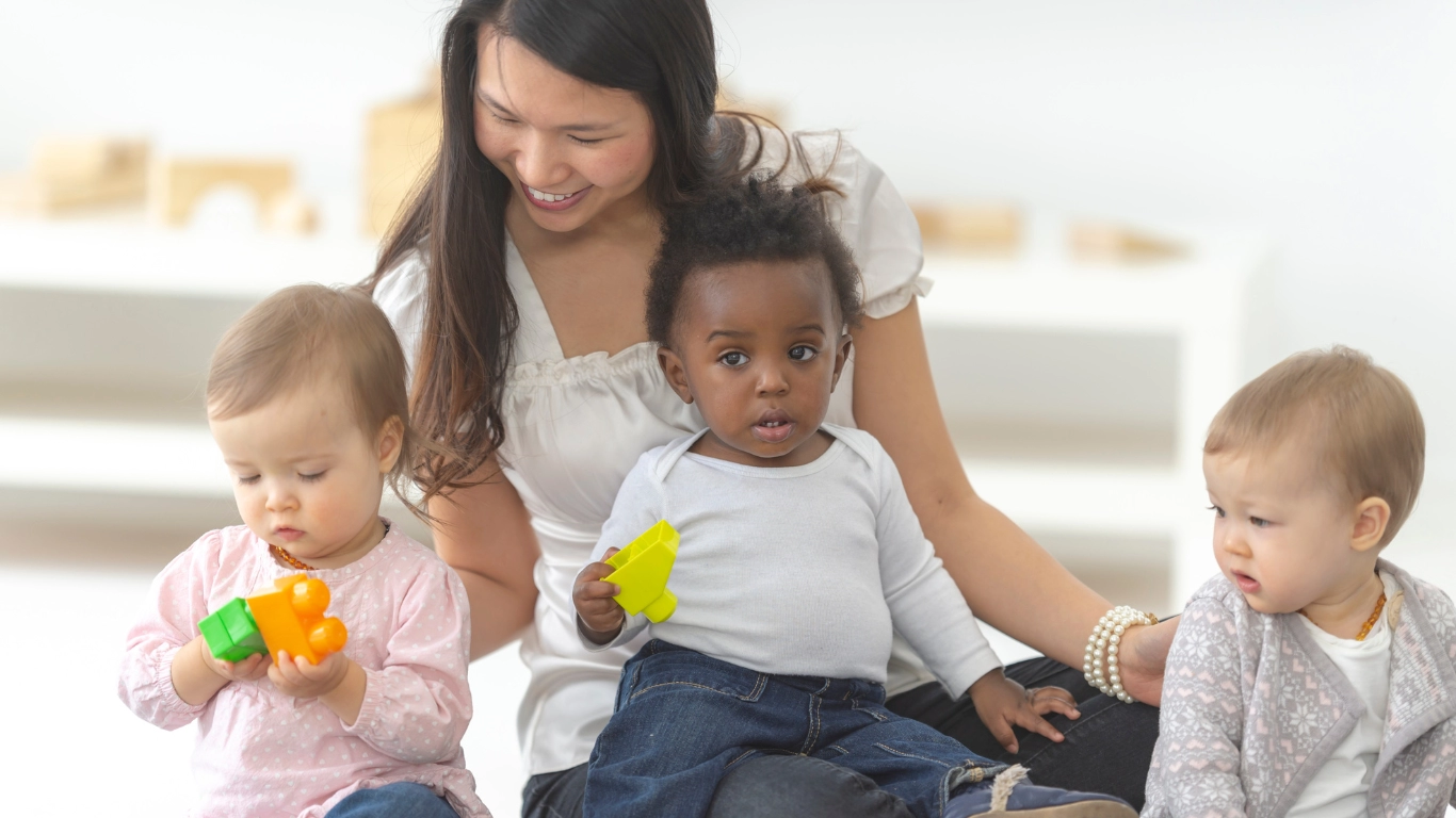 A child care provider interacts with three young children in a calm, nurturing setting—representing the diverse mix of public and private early care and education providers in Los Angeles’s child care system.