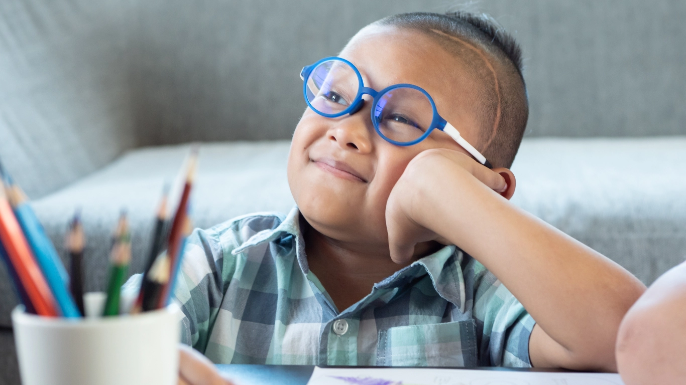 Smiling child with glasses at a table, representing support for children with disabilities.