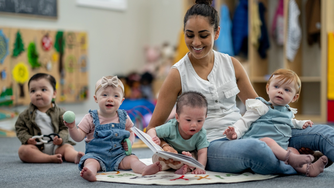 Provider and infants engage with toys and books in a colorful, inclusive classroom setting.